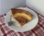 Dutch baby slice on plate with fork, on table with red and white checked tablecloth