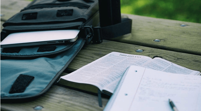 A notebook and a Bible on a bench next to a bag with a laptop