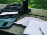 A notebook and a Bible on a bench next to a bag with a laptop
