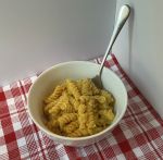 white bowl of mac and cheese with silver spoon on red and white checked table