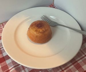 pineapple upside down cake with cherry in center on white plate with a silver fork on it.
