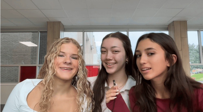 Three young girls speaking into a microphone at the same time, smiling.