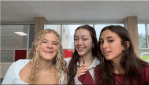 Three young girls speaking into a microphone at the same time, smiling.