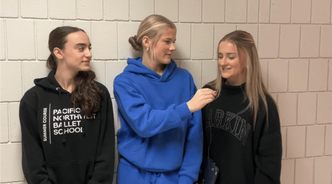 A girl in blues sweats interviewing two other girls in black hoodies.