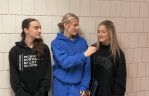 A girl in blues sweats interviewing two other girls in black hoodies.